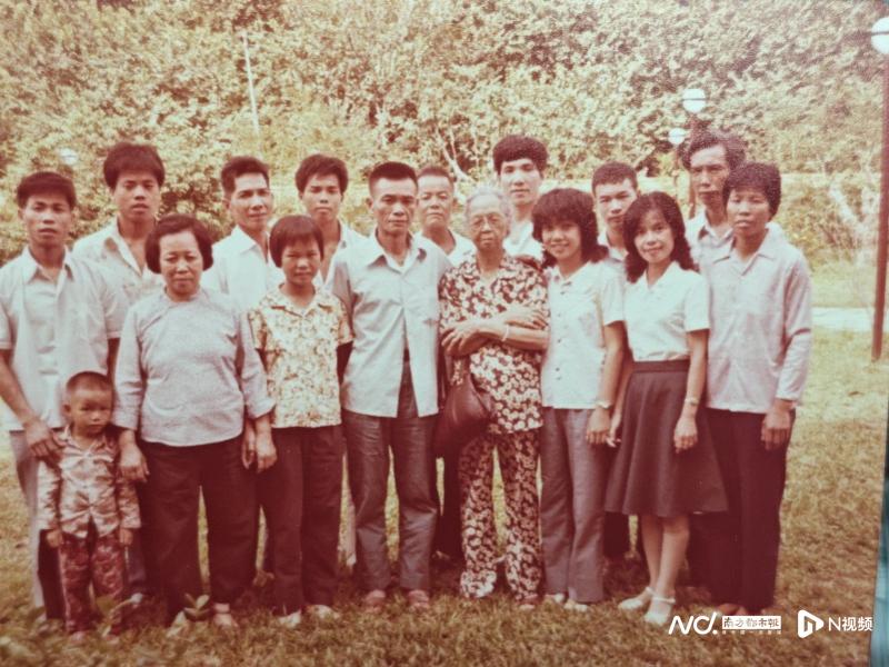 　　郑社心在新加坡家中给南都N视频记者找出母亲钟彩合（前排右四）、弟弟郑社义（前排右五）等家人的合影，这张照片拍摄于上世纪八十年代。